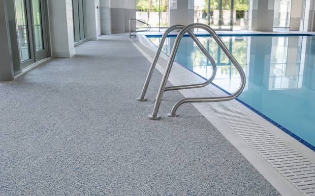Indoor pool deck in pale rubber surfacing with a ladder leading into the water.